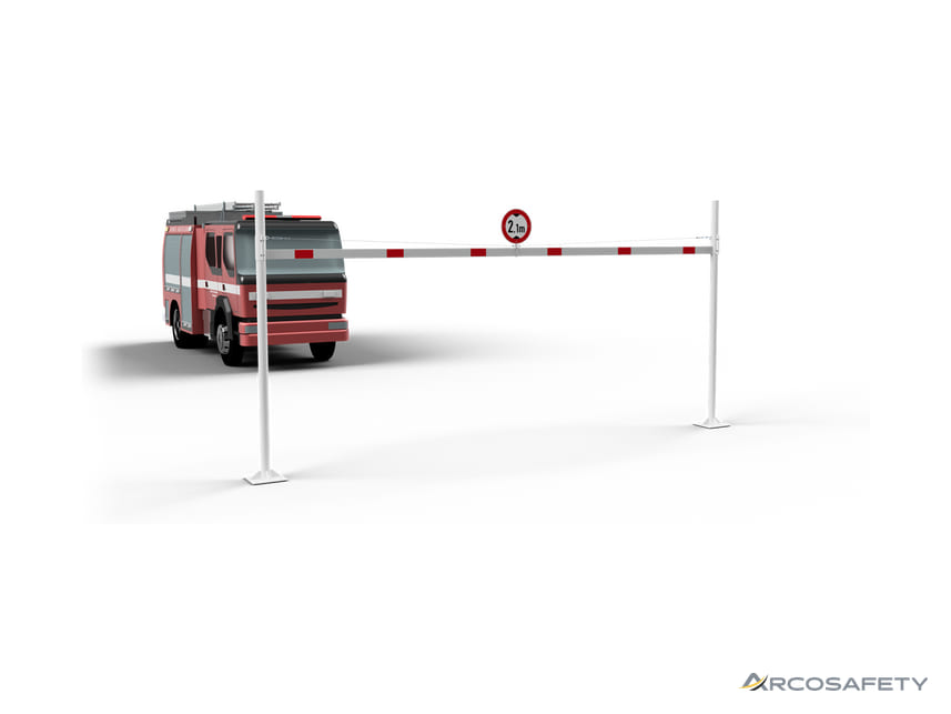 Portale limitatore di altezza bianco a due montanti con traversa a bande rosse, tirante e cartello di altezza massima 2,1 m, davanti a un camion dei vigili del fuoco